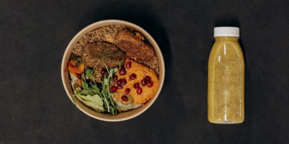 A vibrant vegan bowl with quinoa, fresh vegetables, and a smoothie bottle against a dark backdrop.