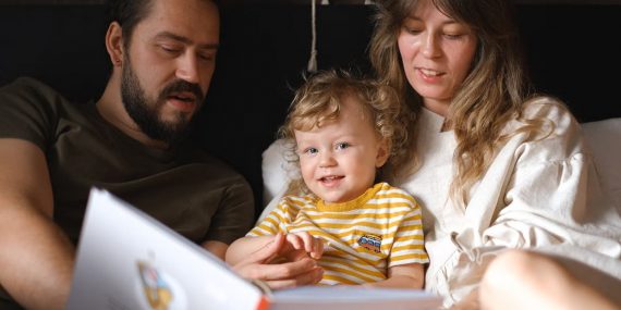 A happy family reading together, featuring parents and their smiling child enjoying a book indoors.